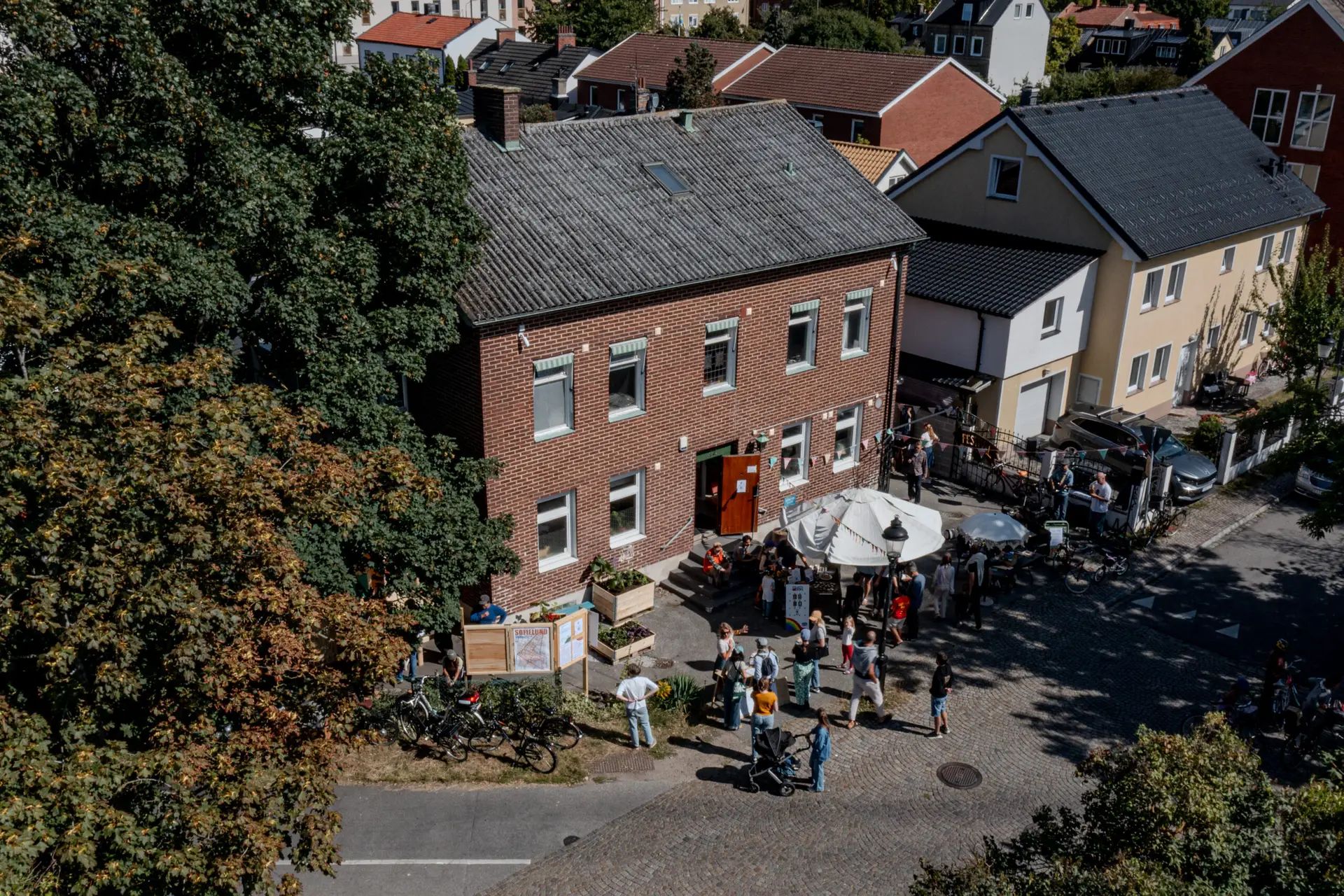 Flygbild över Ödets tegelhus och lummiga bakgård på Idunsgatan 22 i Malmö, fyllt med folk och cyklar under ett kvartersevent. Foto: Andreas Paulsson.