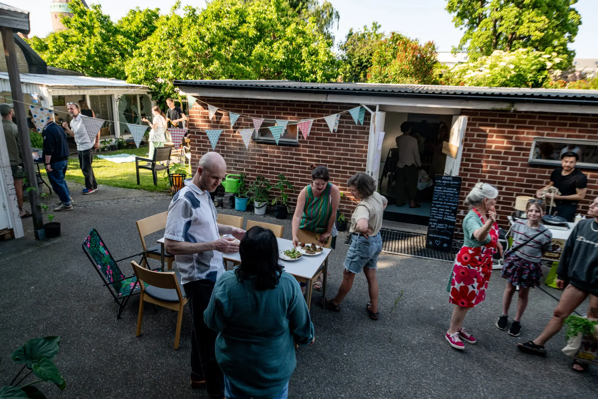 EDeltagare samlas kring ett matbord på Ödets livfulla bakgård fylld med vimplar och lummig grönska. Foto: Andreas Paulsson.