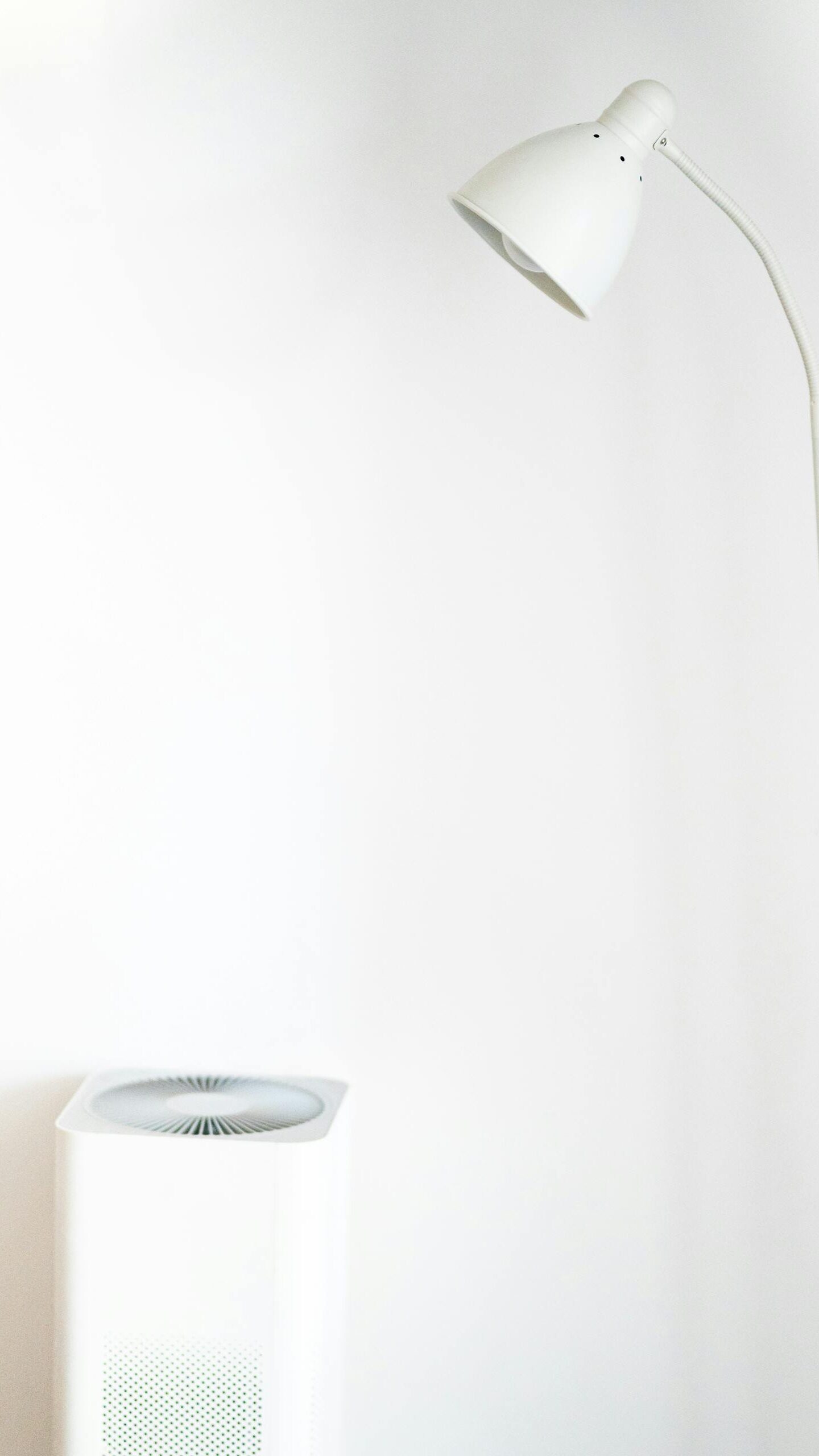 A minimalist room featuring a white floor lamp and air purifier against a blank wall.