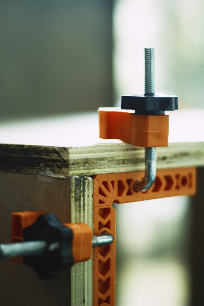 Detailed view of an orange corner clamp used for securing plywood during carpentry work.