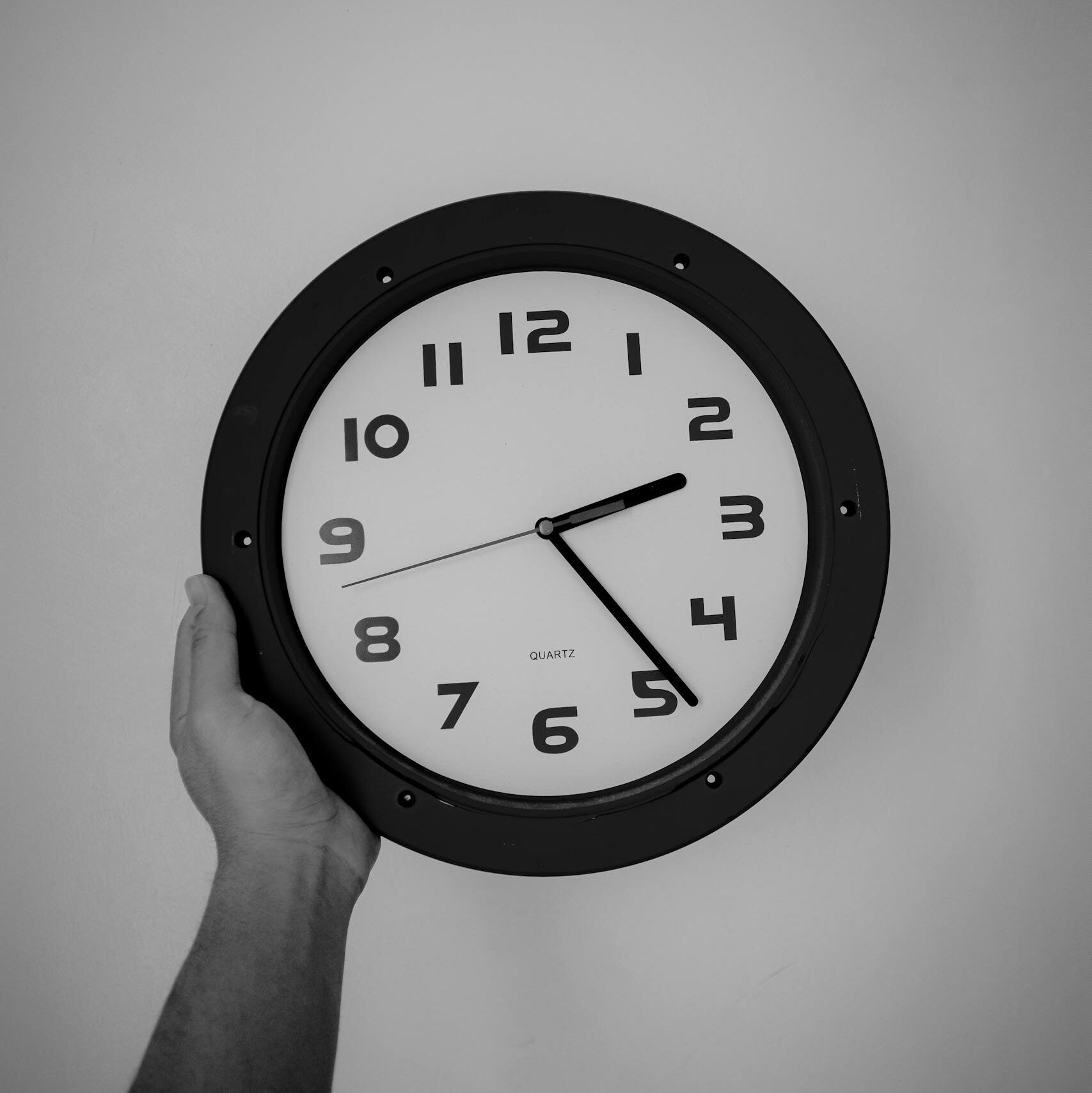 Minimalist black and white photo of a hand holding a wall clock, emphasizing time.