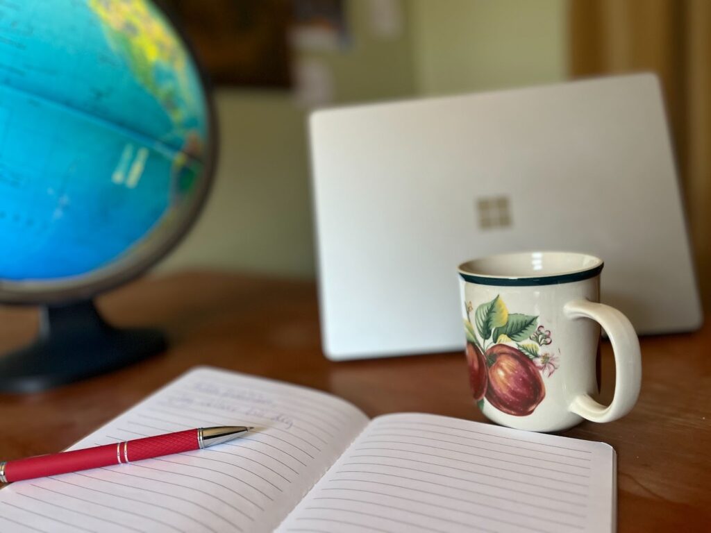 En studie i skrivande och reflektion: anteckningsbok och penna redo för att formulera tankar, med en jordglob i bakgrunden som symboliserar globalt engagemang.