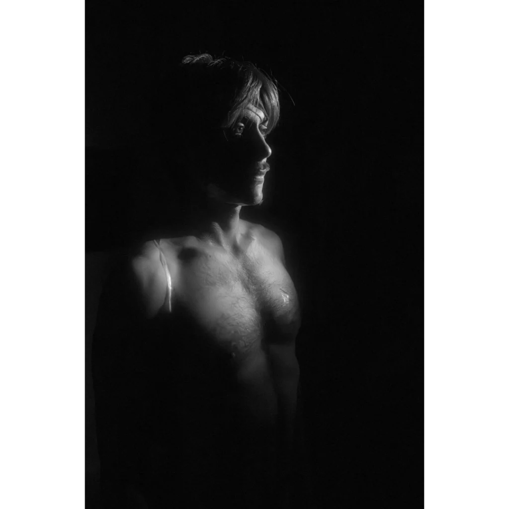 Svartvitt fotografi av en naken performanceartist. Ansiktet och överkroppen framträder delvis ur mörkret, medan genomskinlig tejp syns över bröst och axel. Det dramatiska ljuset skapar stark kontrast mellan det synliga och det dolda. En del av fotograf Andreas Paulssons utställning ”Det Osynliga” visas i samband med Gallerihelgen 2026 på Ödet i Malmö.